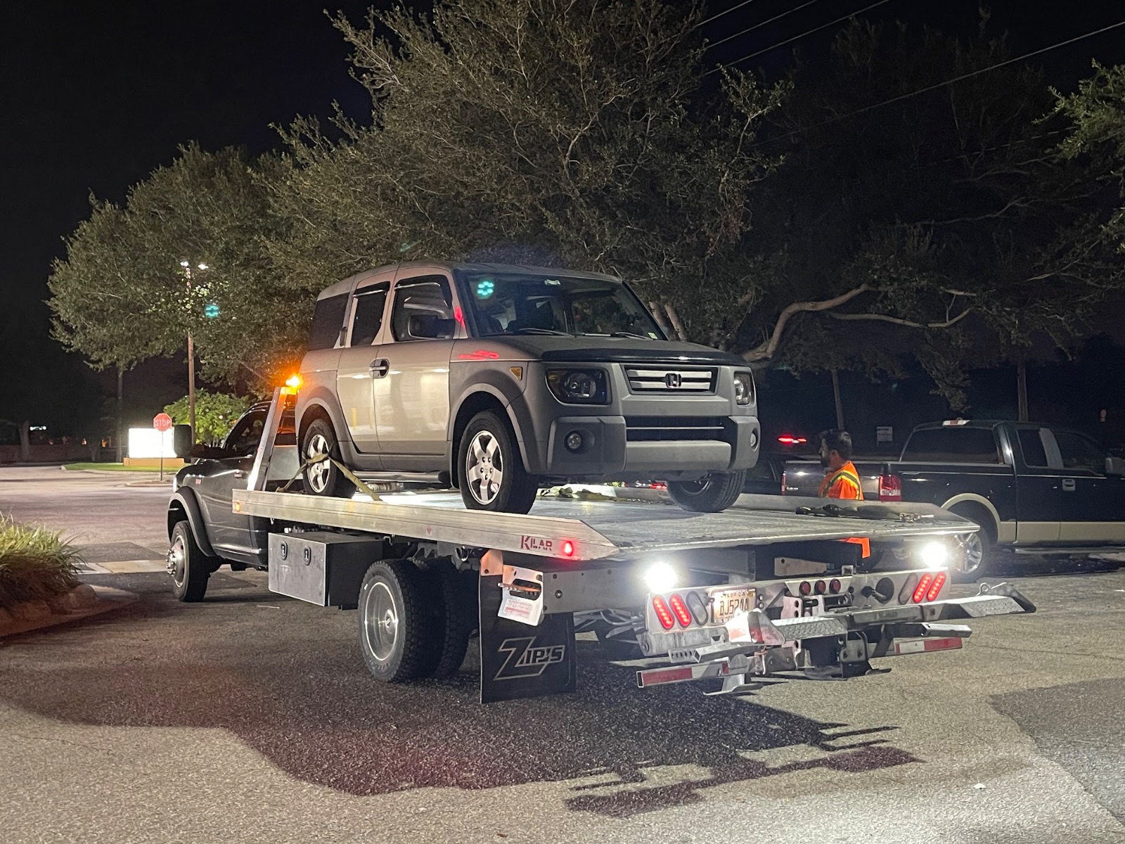 Silver SUV being towed on flatbed truck at night in parking lot