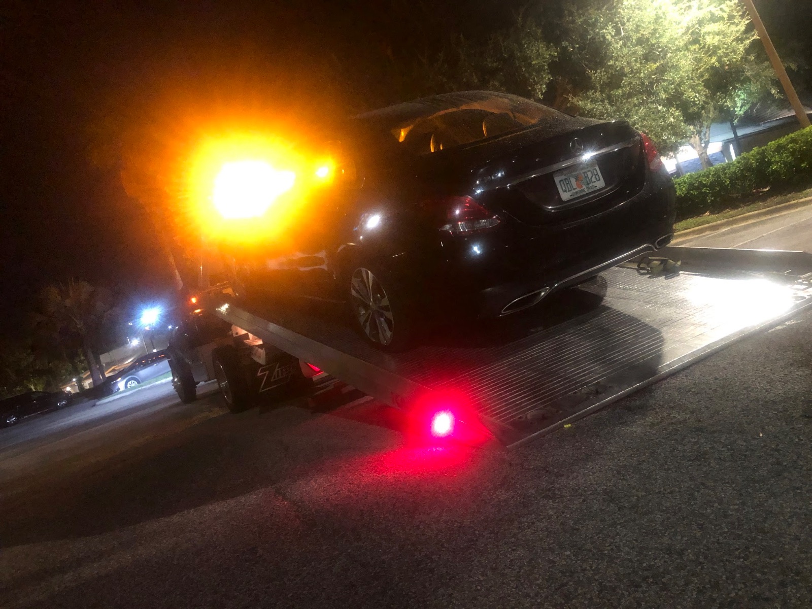 Tow truck loading black sedan at night with illuminated warning lights