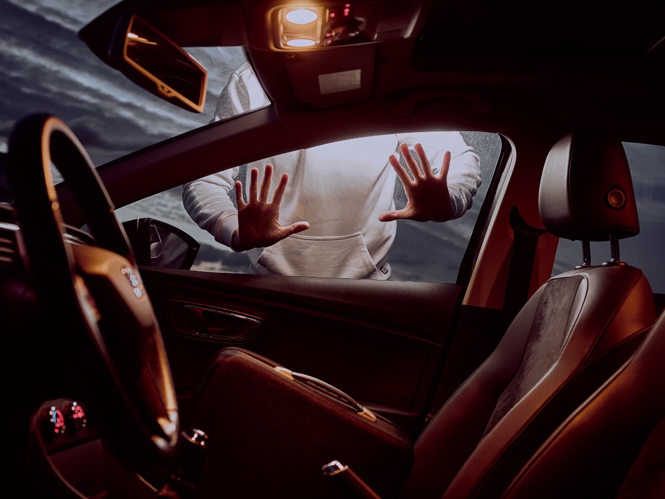 Person with hands pressed against car window from outside, viewed from interior with red leather seats