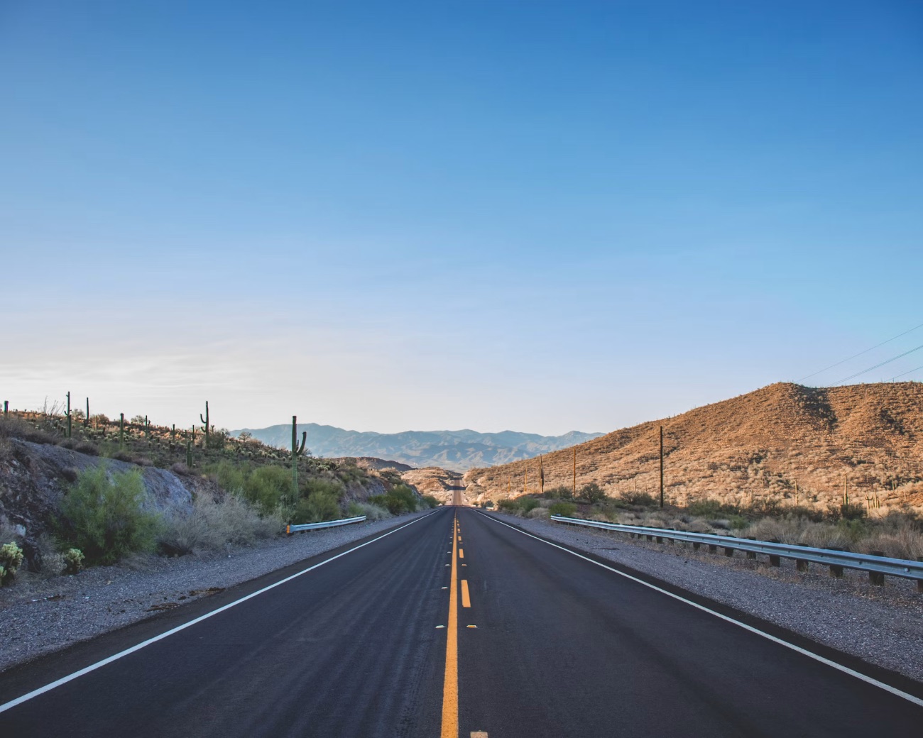 Straight desert highway with yellow center line stretching toward mountains under clear blue sky